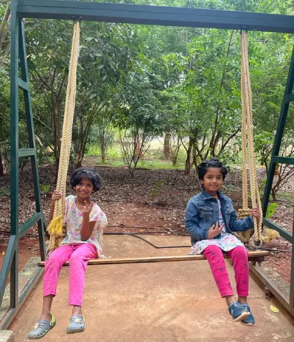 Children enjoying an outdoor rope swing surrounded by trees at a nature retreat near Bangalore